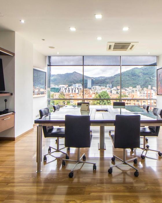 Empty modern meeting room with a glass conference table, office chairs and floor-to-ceiling windows overlooking a city and green mountains